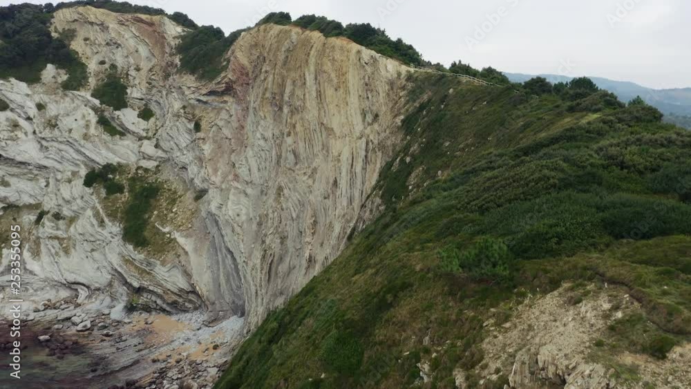 Aerial; drone flight over the steep stone slope of coastal line; eroded rocks and dangerous hillside; tourist route along the edge of ridge; evergreen plants trees and bushes in winter; fog over sea Aerial; drone flight over the steep stone slope of coastal line; eroded rocks and dangerous hillside; tourist route along the edge of ridge; evergreen plants trees and bushes in winter; fog over sea
