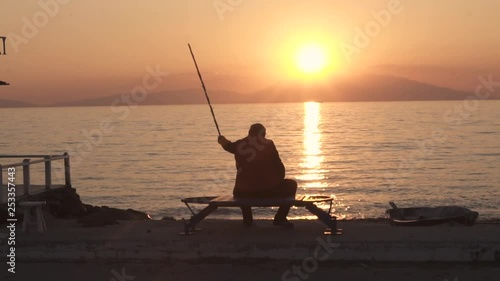 Old Man at the Promenade sitting on bench with a fishing route slow motion photo