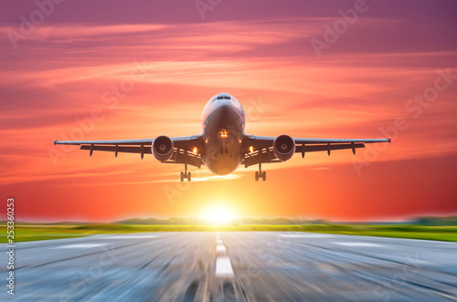 Airplane landing on the runway behind a bright sunset with a pink sky