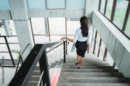 portrait from behind of businesswoman walking down stairs alone in the office