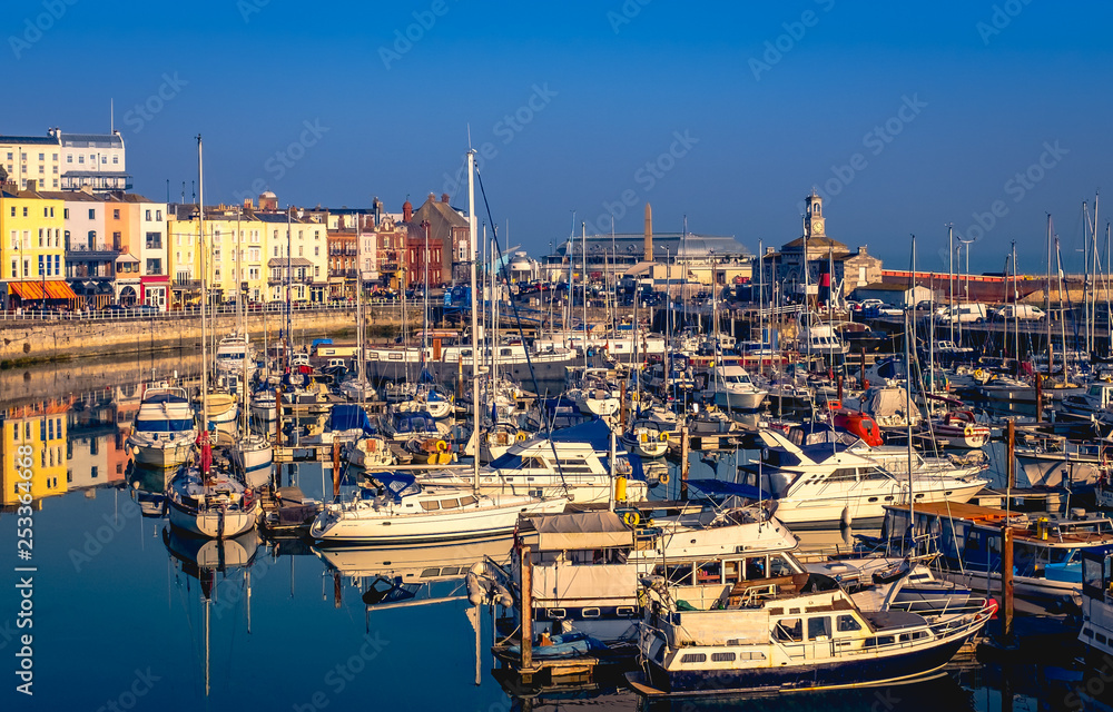 Obraz premium The impressive and historic Royal Harbour of Ramsgate, Kent, Uk, full of leisure and fishing boats of all sizes and the colourful facade of the historic buildings along the marina promenade and clock 