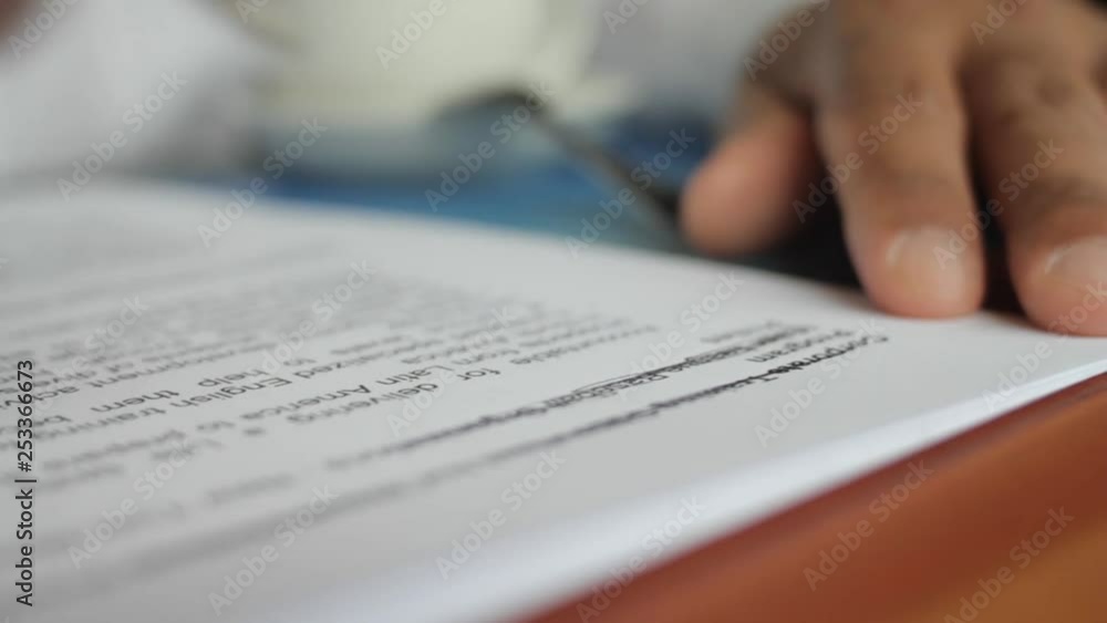 A male hand edits a printed document with a pen on a wooden table. A male hand edits a printed document with a pen on a wooden table.