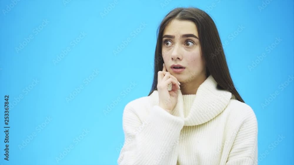 Picture of happy young lady standing on a blue background. Look into the camera. During this time she is dressed in a white warm sweater. With long black hair. Picture of happy young lady standing on a blue background. Look into the camera. During this time she is dressed in a white warm sweater. With long black hair.