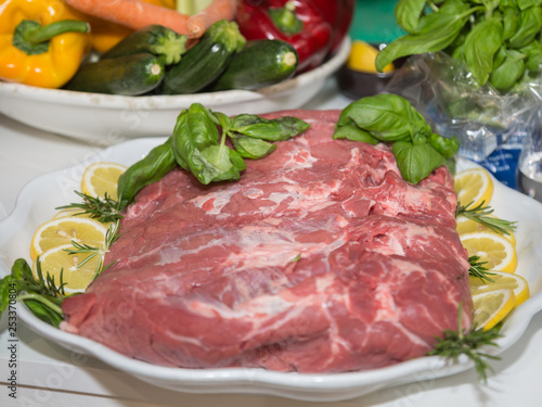 Piece of Raw Beef on a Plate Garnished with Slices of Lemon and Basil and Rosemary