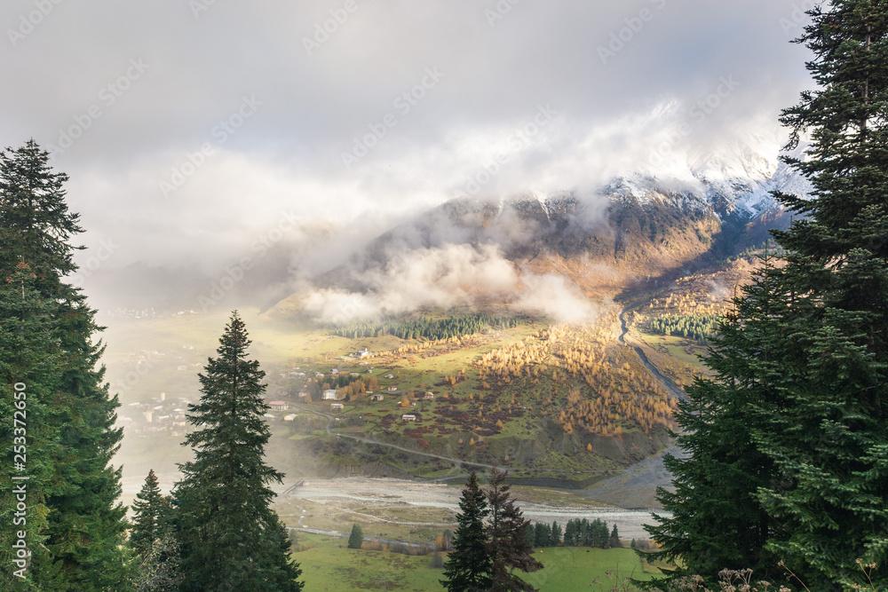 Panoramic view of small town placed on green hills of mountain valley in clouds, Svaneti 