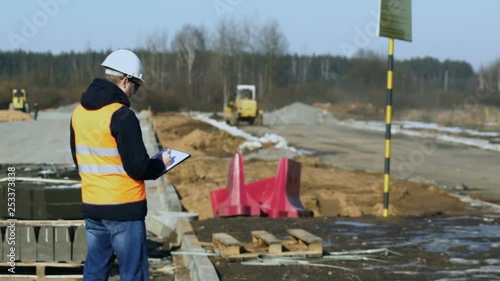 Engineer inspector looks and writes data during a phase of road construction before laying of pavement material or roadbed