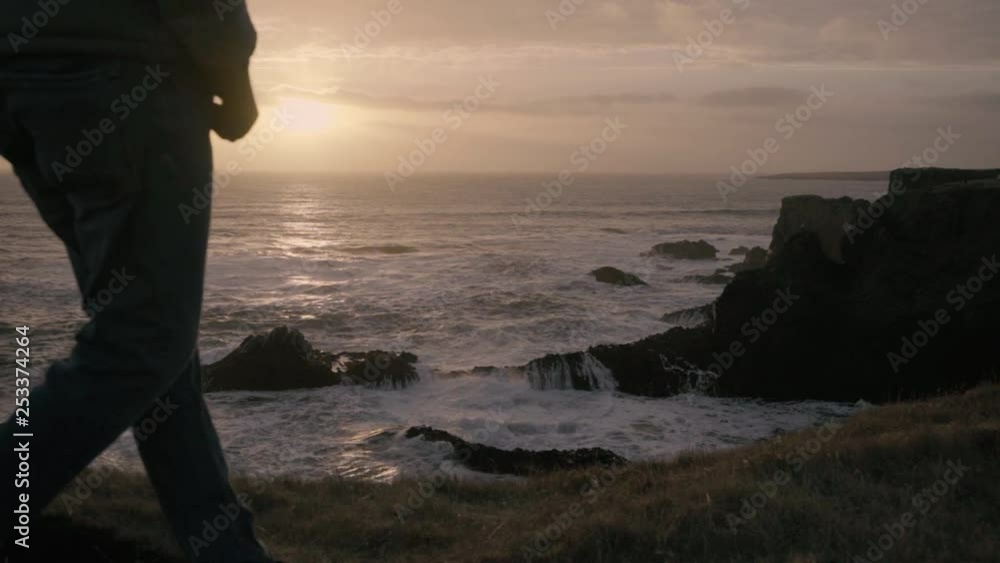 Slowmo shot during sunset, showing waves hitting the coast, with a man stepping in the frame. Slowmo shot during sunset, showing waves hitting the coast, with a man stepping in the frame.