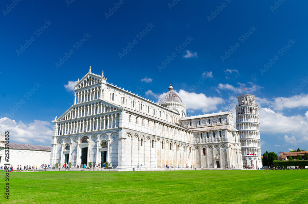 Pisa Cathedral Duomo Cattedrale and Leaning Tower Torre on Piazza del Miracoli square green grass lawn, blue sky with white clouds copy space background in sunny day, Tuscany, Italy