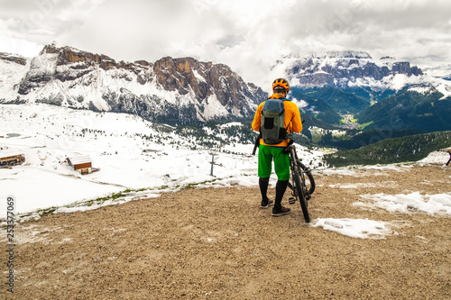 Cyclists standing backwards and watching at beautiful Dolomites mountains covered with snow in South Tyrol, Italy. Alpine activities, mountainbing with amazing nature view