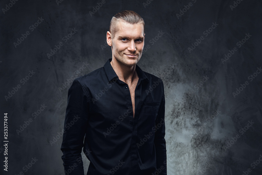 Fashion portrait of handsome with perfect haircut and unbotton black shirt looking at a camera. Studio shot on a dark textured wall