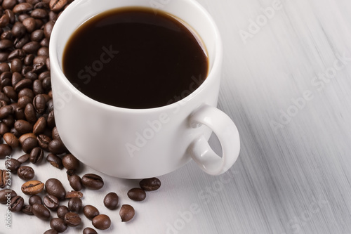 a cup of black natural coffee, coffee beans, on a light wooden table