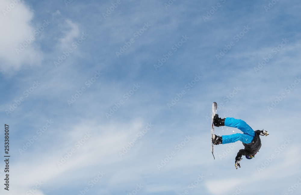 Snowboarder (boy, male) doing an acrobatic backflp after a jump.  With copyspace and blue sky.