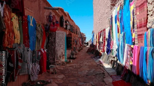 Slowmotion walking through a street in a small Moroccan village, scarves being sold on both sides.