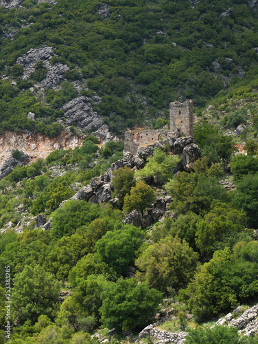 Stone tower ruins on a steep rocky cliff with trees in Mani, Greece.