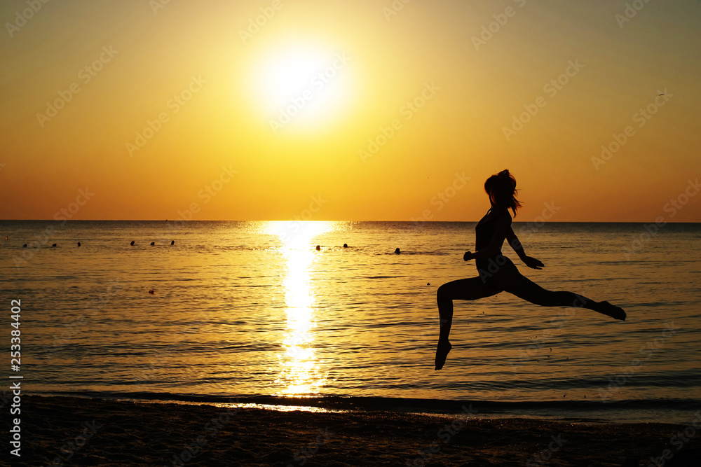 silhouette of a girl in a bathing suit running along the beach on the background of the dawn