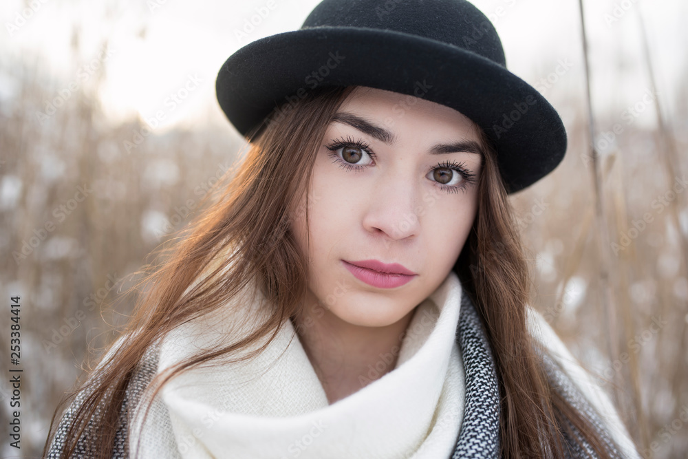 Portrait of natural beauty brunette woman with big brown eyes, and bowler hat on, in winter scenery. Blurred background with meadow cover by snow. Portrait of natural beauty brunette woman with big brown eyes, and bowler hat on, in winter scenery. Blurred background with meadow cover by snow.