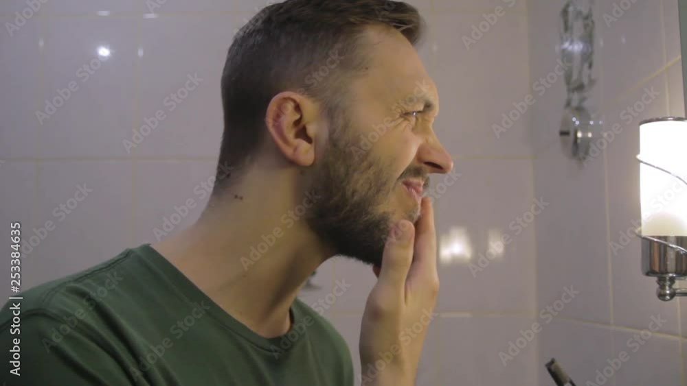 Side view on young man in bathroom looking at the mirror, checking face for skin diseases Side view on young man in bathroom looking at the mirror, checking face for skin diseases