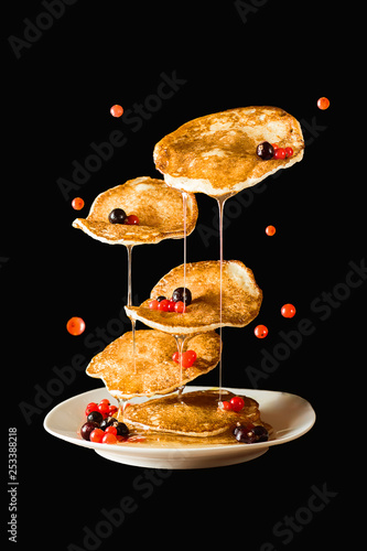 Flying pancakes with honey and currant. Black background.