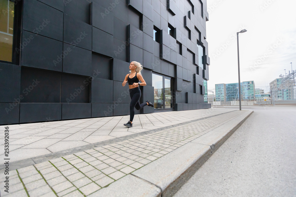 Focused fast running woman wearing sports top in modern city environment