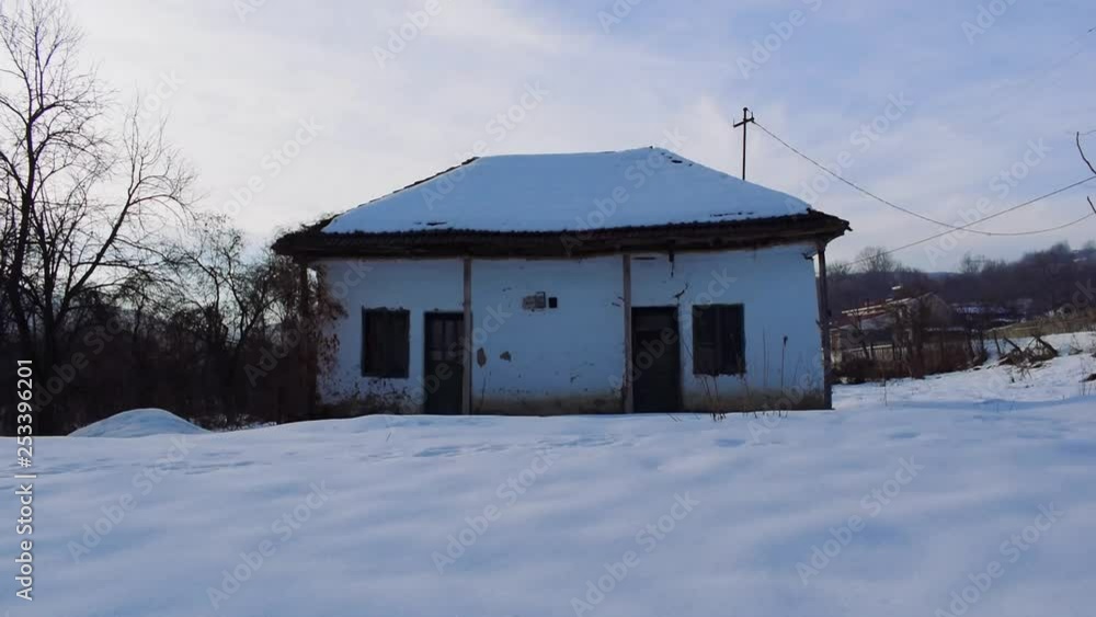 Camera tilts down from sky to ground revealing old, snow covered white cottage in a snow covered field. Camera tilts down from sky to ground revealing old, snow covered white cottage in a snow covered field.