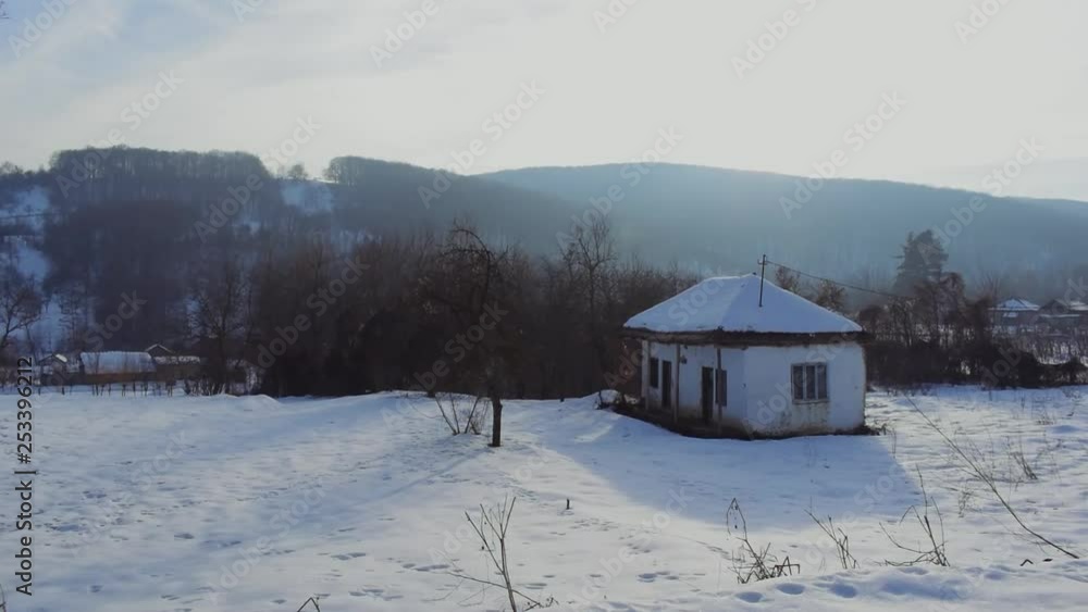 Camera pans right to left looking towards small whites no-covered cottage in a snowy field then finishes at lone tree. Camera pans right to left looking towards small whites no-covered cottage in a snowy field then finishes at lone tree.