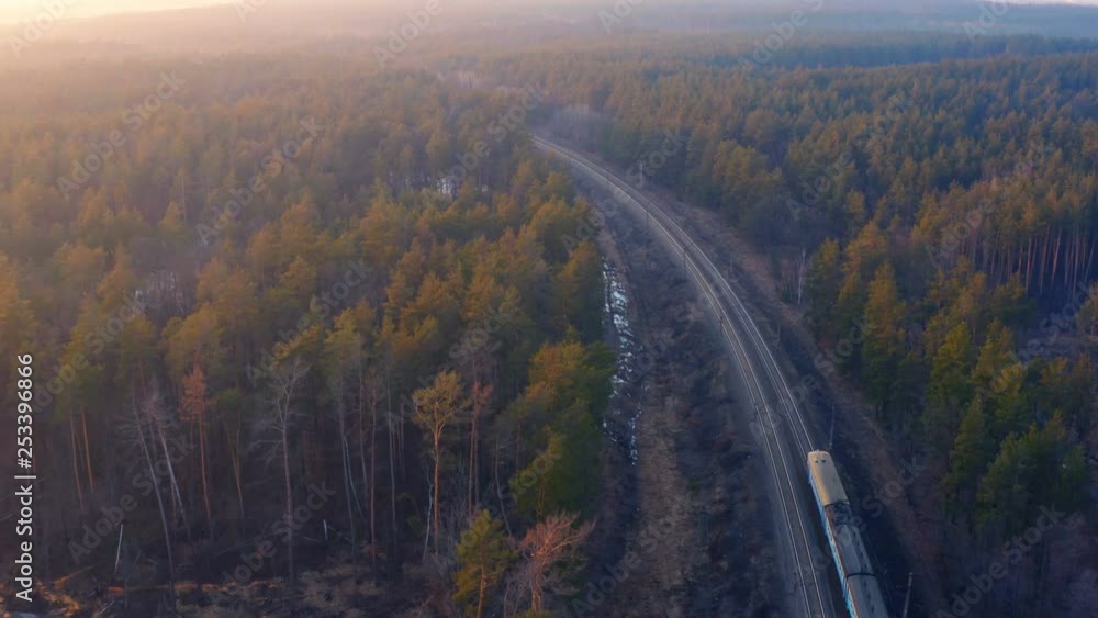 Aerial view of the suburban train (commuter rail) rides through the spring forest at sunset Aerial view of the suburban train (commuter rail) rides through the spring forest at sunset