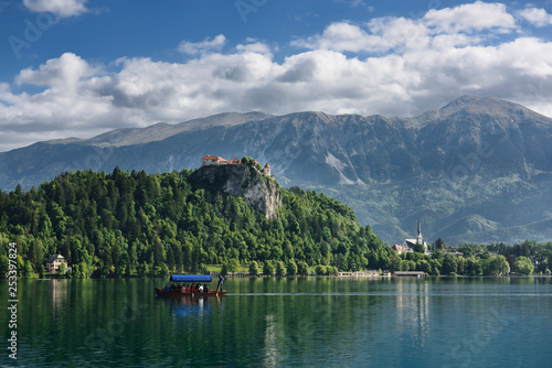 Traditional Pletna boat rowing tourists on Lake Bled with Bled castle on cliff and St Martin church Sol massive of Karawanks mountains Slovenia
