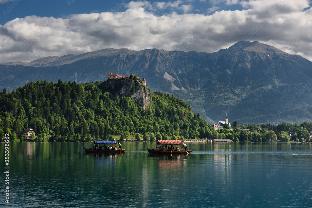Traditional Pletna boats with colorful canopy on Lake Bled with Bled castle on cliff and St Martin church Sol massive of Karawanks mountains Slovenia