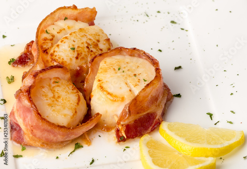 Bacon Wrapped Scallops on White Plate with Lemon Slices and Green Garnish