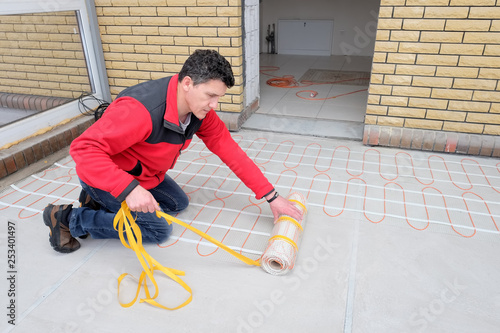 Electrician installing heating electrical cable on concrete floor. Man remove adgesive tape.