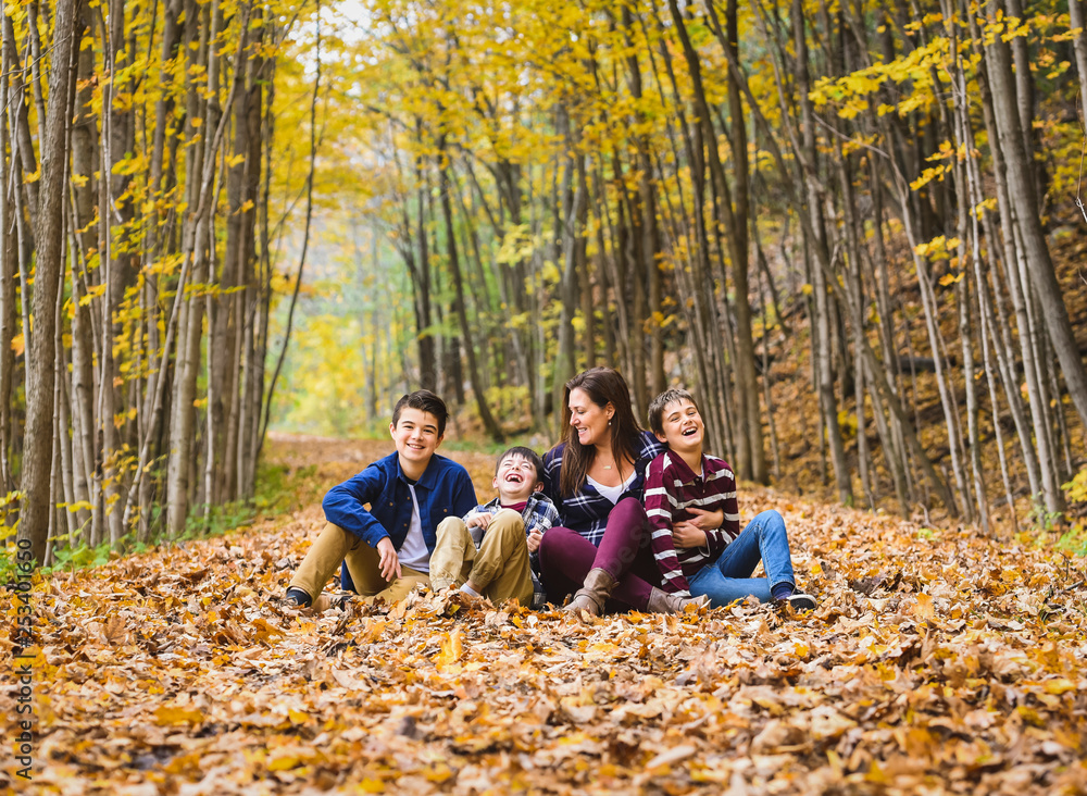 Playful mother sitting with sons on dry leaves in forest Playful mother sitting with sons on dry leaves in forest