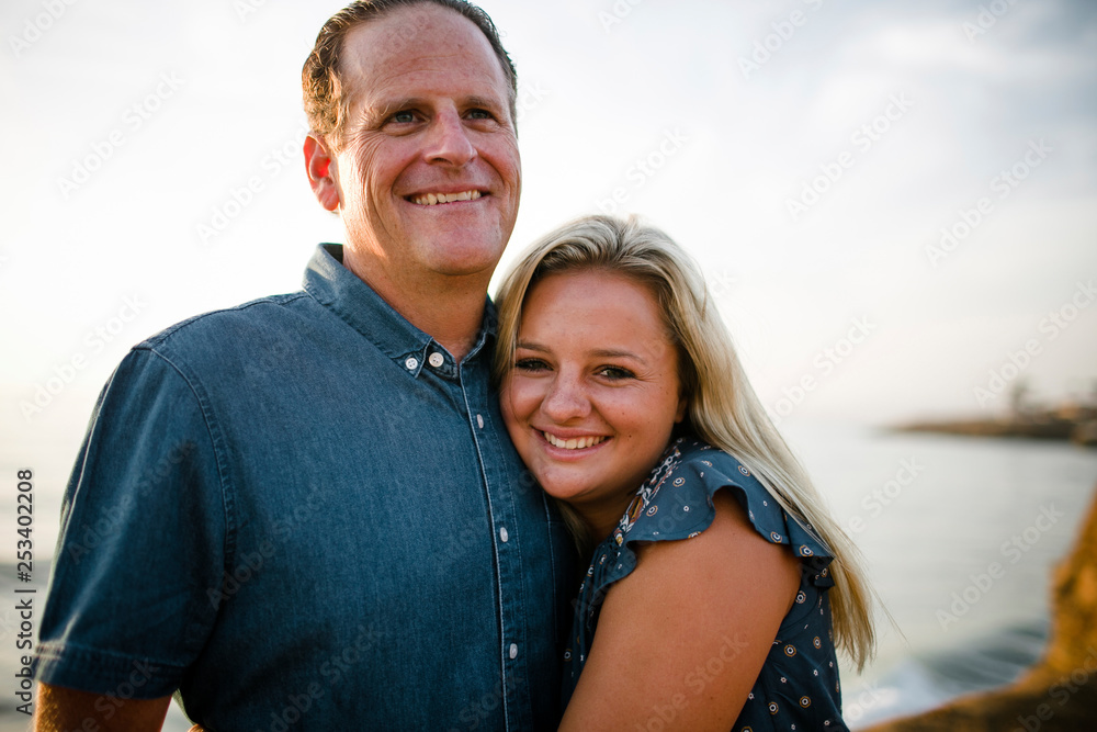 Portrait of happy daughter embracing father while standing on cliff against sky during sunset Portrait of happy daughter embracing father while standing on cliff against sky during sunset