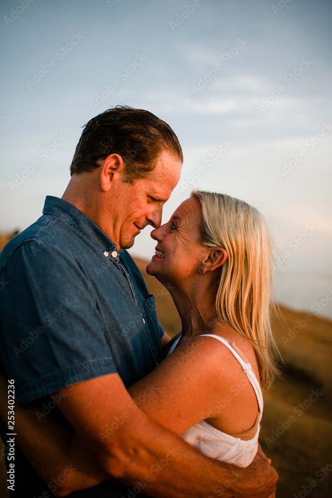 Side view of romantic couple looking at each other while standing on cliff against sky during sunset