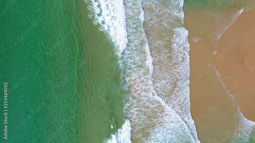Static aerial top down view of beautiful sandy beach with clear turquoise ocean water including people swimming in small waves. Static aerial top down view of beautiful sandy beach with clear turquoise ocean water including people swimming in small waves.