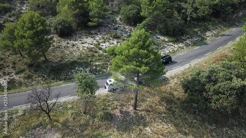 Two Cars standing on a mountain pass. Filmed from top bird's eye view with a drone smooth tilt motion. Summer atmosphere in green forrest und grey rocky french alps landscape photo