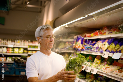 Mature man holding up a lettuce at a grocery store. photo