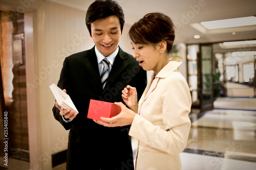 Young adult businessman giving a gift to his girlfriend in a lobby.