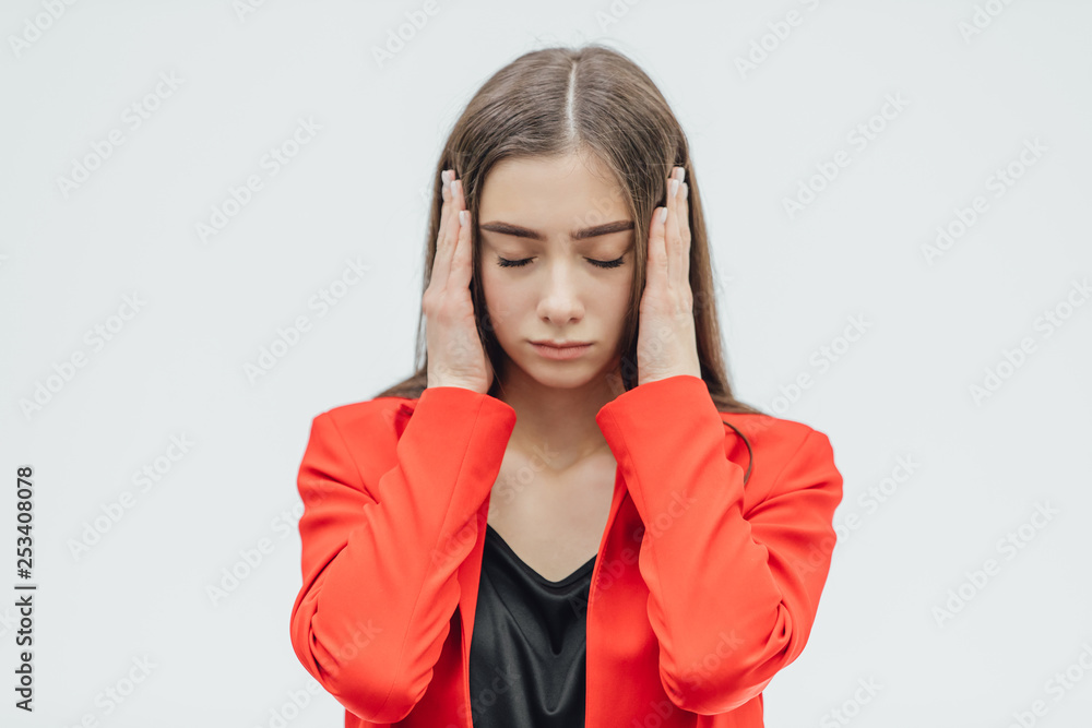 Portrait of a beautiful young brunette with open shoulders, touching her temples feeling stress, on a gray background. Portrait of a beautiful young brunette with open shoulders, touching her temples feeling stress, on a gray background.