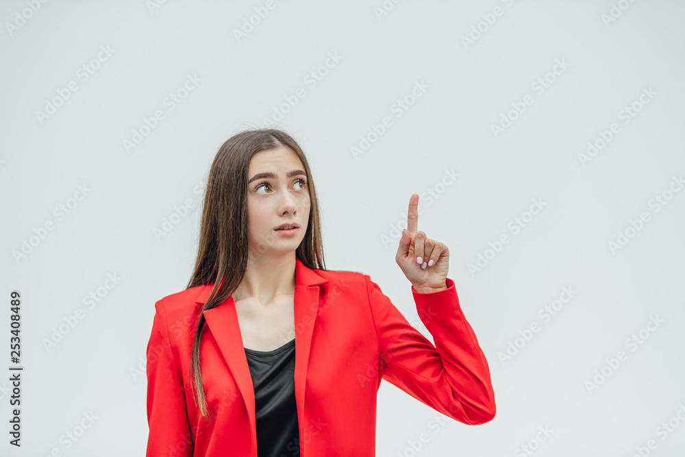 Portrait of a beautiful young brunette. Look into the camera. During this, the girl raised her hand with her index finger up. Dressed in a red jacket. Portrait of a beautiful young brunette. Look into the camera. During this, the girl raised her hand with her index finger up. Dressed in a red jacket.