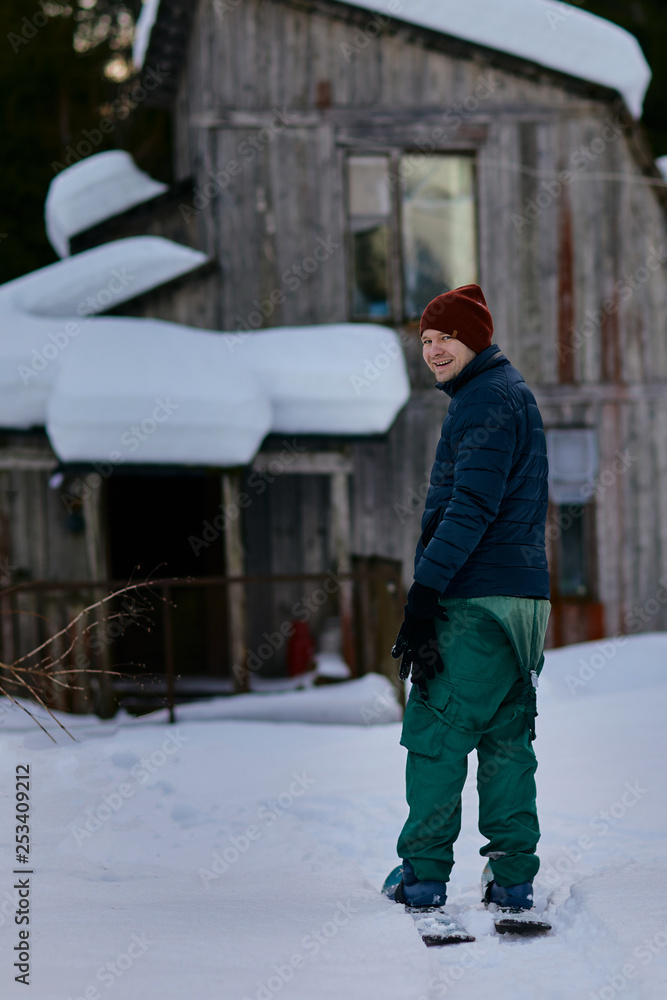 A man stands on skis in the forest on the background of an old wooden house.