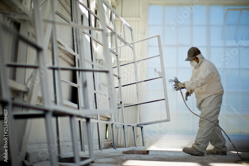 Mid adult man in protective clothing spray painting window frames inside a garage.