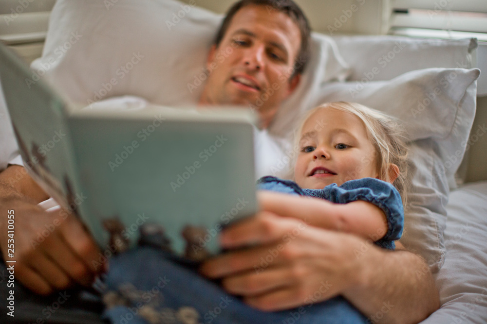 Father lying down reading a book with his daughter. Father lying down reading a book with his daughter.