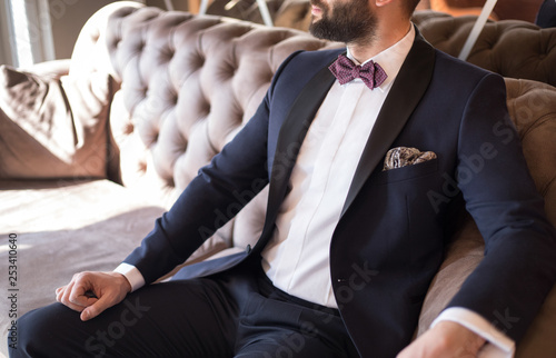 Photo Man in expensive custom tailored suit, tuxedo with bow tie siting and posing on
