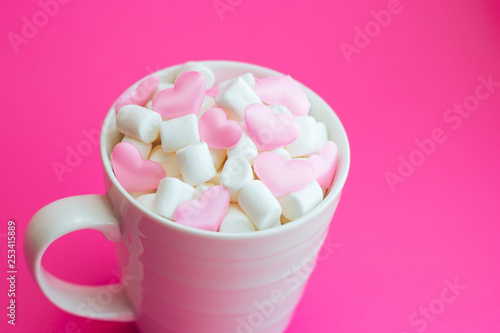 Mug with marshmallows in the shape of heart on pink background