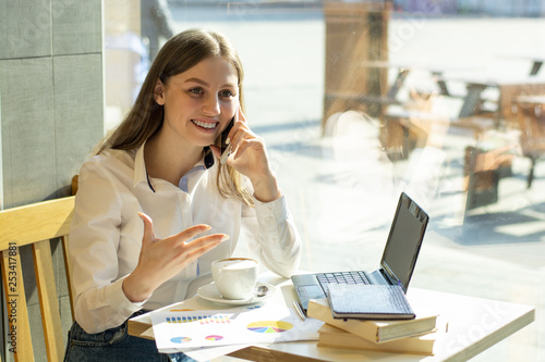 beautiful girl businesswoman in a cafe writing in a notebook talking on the phone