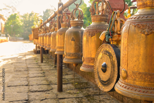 Outdoor scenery with sunshine at temple in Chiang Mai, Thailand, and selective focus view row of hanging antique brass bells, traditional religious instrument for asian and buddhism culture.