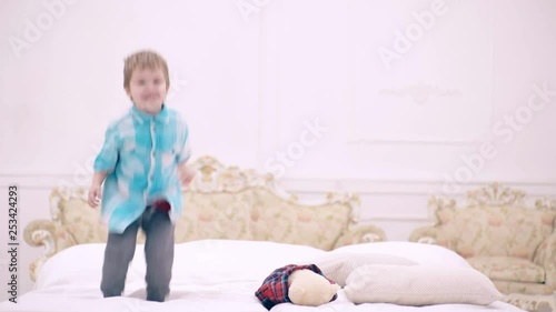 Happy little boy jumping on bed in bedroom. cute little child or toddler jumping happily at home. Curly baby boy on bed jumps before going to bed. Child is happy and fun in parents bedroom.