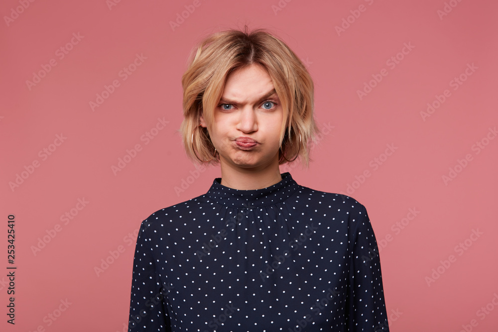 Blonde girl offended angry upset, pouted her cheeks is overwhelmed with negative emotions, in bad mood dressed in blouse with polka dots,isolated on pink Blonde girl offended angry upset, pouted her cheeks is overwhelmed with negative emotions, in bad mood dressed in blouse with polka dots,isolated on pink