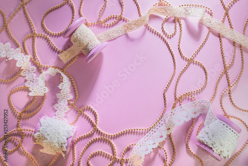 Pink reel with white lace ribbon. Pearls lie on a pink background. Golden beads scattered around the table. Flat lay. A place for your inscription. Background for site design, landing page or blog.