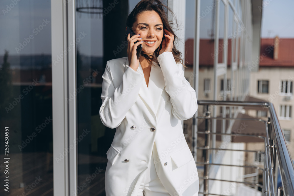 Pretty stylish business woman stands on the balcony near modern office and talking on the smartphone. Pretty stylish business woman stands on the balcony near modern office and talking on the smartphone.